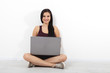 © missty - Happy young woman sitting on floor with crossed legs and using laptop on white background