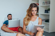© jakubzak - Young couple is sitting on the bed while using notebook and pc t