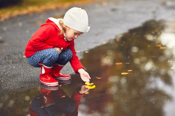 Wall Mural - happy child girl playing with autumn leaves in a puddle after a