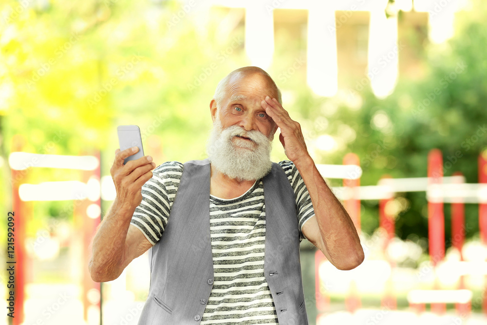 Elderly bearded man with modern phone in park on sunny day