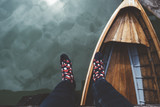 Fototapeta Do pokoju - View of legs and feet with socks on Braies lake with wood boat