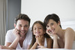 © PhotoAlto - Parents and daughter lying on bed together, portrait