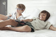 © PhotoAlto - Children using remote control while lying on bed