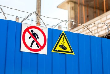 Warning signs and barbed wire on the fence at the construction s