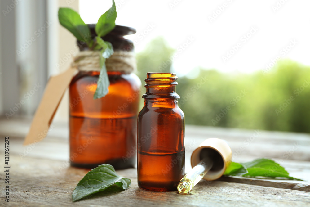 Bottles with mint oil and fresh leaves on blurred natural background