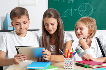 Wall Mural - Schoolchildren with tablet computer sitting at table in classroom