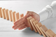 Male hand stopping domino effect on wooden table