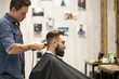 © fizkes - Side view portrait of handsome young bearded caucasian man getting trendy haircut in modern barbershop. Cool men hair stylist with tattoo 'born barber' serving client. Indoors shot