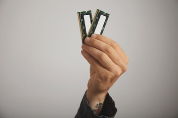 Close up of a tattooed man's hand with two RAM planks with chips against white wall background