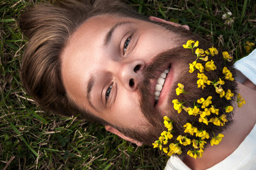 Man with flowers in his beard lying on the green grass