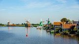 Fototapeta Tęcza - View from the Zaan River of old Dutch Windmills and historic houses along the river at the historic villages of Zaanse Schans and Zaandijk in the Netherlands