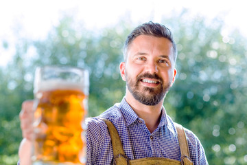 Wall Mural - Man in traditional bavarian clothes holding mug of beer