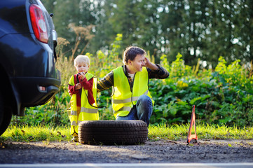 Father and his little son repairing car and changing wheel together