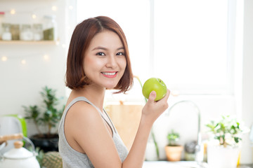 Wall Mural - Happy Young Asian Woman Eating Green Apple on Kitchen. Diet. Die