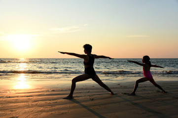 Wall Mural - Yoga Virabhadrasana II (Warrior II Pose) by mom and daughter in silhouette with sunset sky background