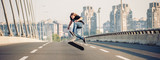 Skater doing tricks and jumping on the street highway bridge, through urban traffic. Free riding skateboard. Panorama view