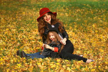 Portrait of smiling beautiful young woman and her little daughter sitting on grass autumn