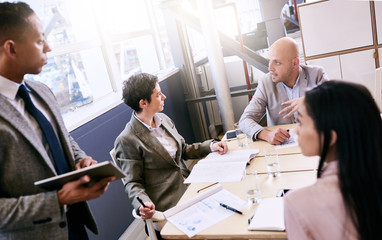 Professional mature adult mixed race well dressed businessman conducting a presentation in a bright modern conference room while holding and using a tablet in his presentation.