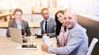 © nakophotography - four business professionals all looking at the camera during a business meeting in a modern conference room with a large window behind them with bright natural light coming in.