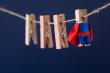 Powerful super hero conceptual photo with superstar clothespin character in blue suit red cape. leadership and wooden clothespins team at work. Dark blue background.