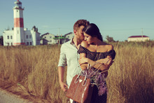 Young Couple Hipster Indie Style In Love Walking In Countryside, Gentle Hugs, Lighthouse On Background, Warm Summer Day, Sunny, Bohemian Outfit, Vintage Bag With Flowers