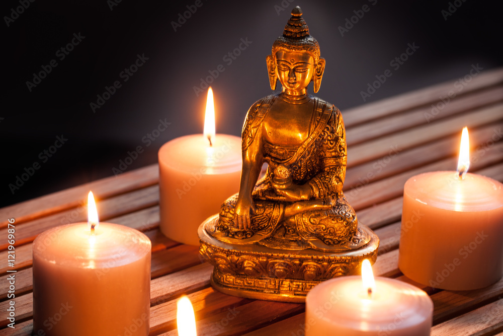 Photographie Bronze Buddha with warm lighted candles over wooden background