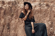 © zolotareva_elina - beautiful woman in black dress and hat posing at stone wall back