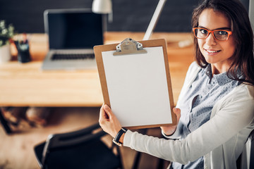 Young woman standing near desk with laptop holding folder