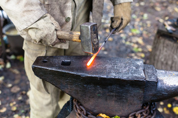 Blacksmith hammering hot steel rod on anvil