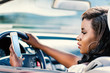 African girl driving car with smart phone in hand.
