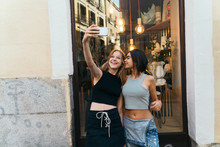 Cheerful Girlfriends Using Mobile Against Shop-window