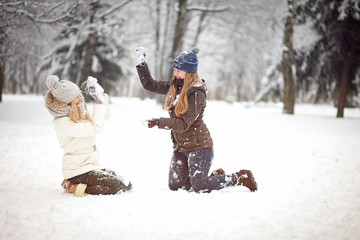 Two girls friends or sisters playing snowballs in the snow in the winter in a warm winter clothes