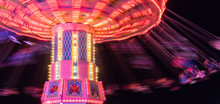 People  Spinning Around Fast And High In Swings At The Brightly Lit Ride At The County Fair 
