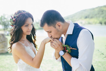 happy groom in a dark blue suit kisses the hand of his beautiful bride in a white wedding dress outdoors. focus on bride