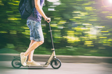 Female Rides A Scooter At Speed Down The Road, Blurred Background The Green Trees