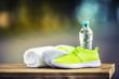 Pair of yellow green sport shoes towel water smart pone and headphones on wooden board. In the background forest or park trail.Accessories for running sport.