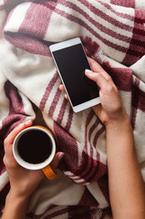 Wall Mural - Hands holding coffee and phone in warm bed on autumn time