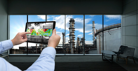 Wall Mural - Industry 4.0 concept .Man hand holding tablet with Augmented reality screen and automate wireless Robot arm software at industrial room in smart factory.Window showing oil refinery industry background