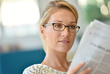 Middle-aged Blond Woman With Eyeglasses Reading Newspaper