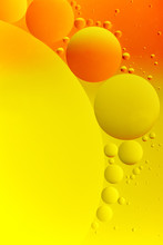 High Contrast Abstract Of Oil Droplets On Water. Small Yellow And Orange Droplets Are Grouped Around A Large Drop. 