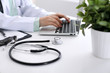 © rogerphoto - Close-up of stethoscope is lying on the table near female doctor typing on laptop computer