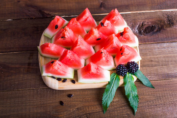 Wall Mural - Triangular pieces of watermelon with seeds, blackberries and mint on a wooden board. On a wooden background.