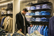 Side view of young male customer choosing shirt in menswear shop