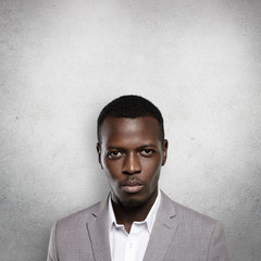 Portrait of successful confident dark-skinned entrepreneur wearing gray formal suit, standing against studio wall with copy space for your text or promotional content, looking serious and thoughtful