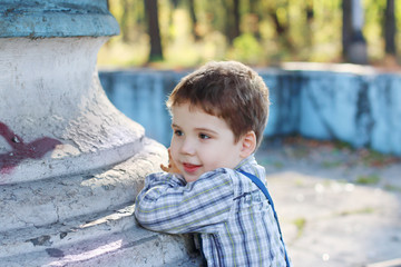 Handsome little boy with bow tie stands near old fountain in par