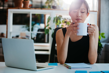 Wall Mural - Relaxed young woman having coffee at her desk