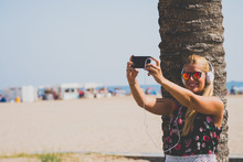 Smiling Blonde Girl Makes Selfie On Beach