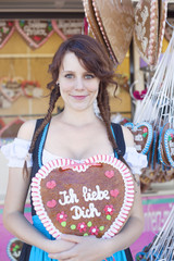 German girl wearing a Dirndl and holding a traditional Oktoberfest's gingerbread heart