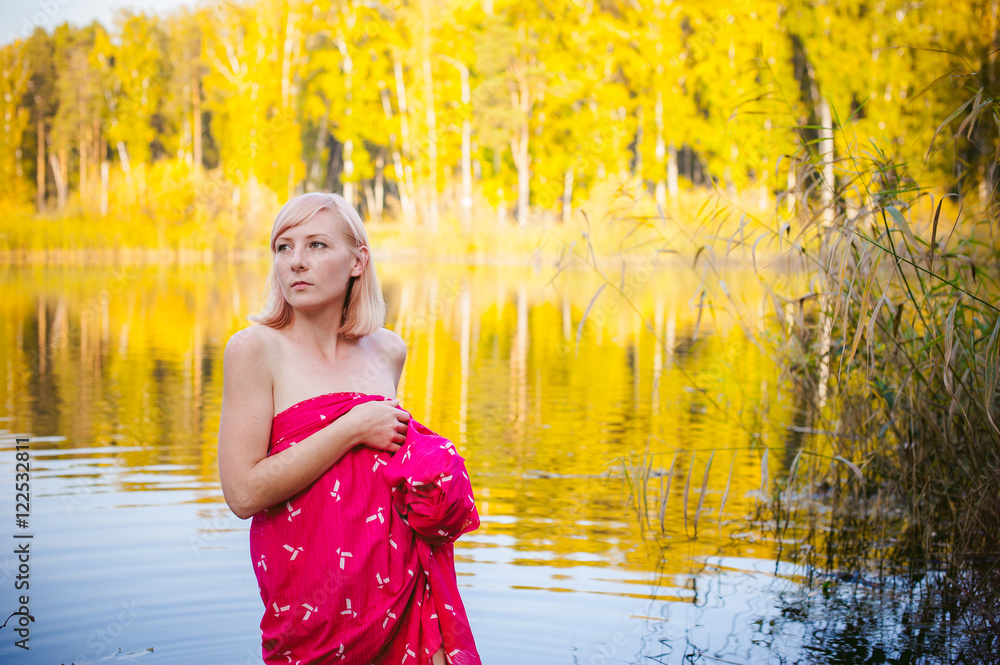 nude girl in sedge. young blonde woman with bare breasts, wrapped in a red cloth, standing in