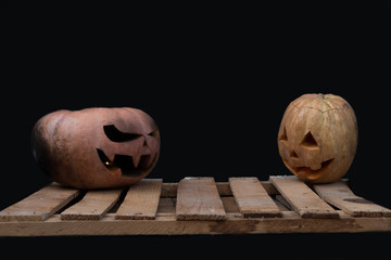 Two Halloween pumpkins on the boards against each other on a black background